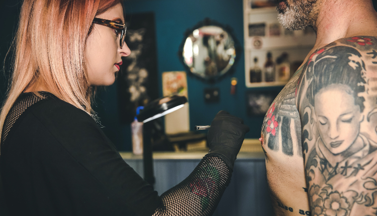 woman tattooing male client